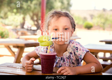 Fun cute thinking kid girl drinking smoothie juice with serious look in summer cafe. Closeup portrait Stock Photo