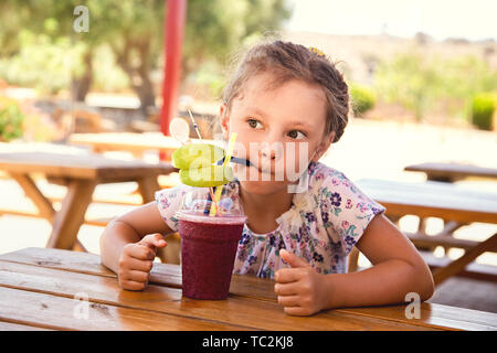 Fun cute thinking kid girl drinking smoothie juice with serious look in summer cafe. Closeup portrait Stock Photo