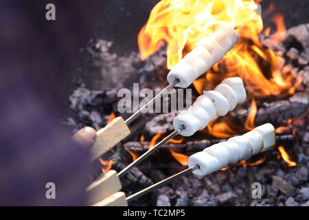 Man toasting marshmallows threaded on metal skewers on a fire for dessert at a summer barbecue or picnic Stock Photo