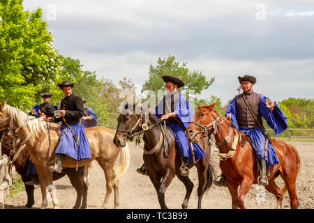 Kalocsa, Puszta, Hungary - May 23, 2019 : Hungarian Csikos horsemen displaying riding skills in traditional costume in countrside corral. Stock Photo