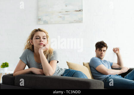 selective focus of upset blonde woman sitting on sofa near man after quarrel Stock Photo