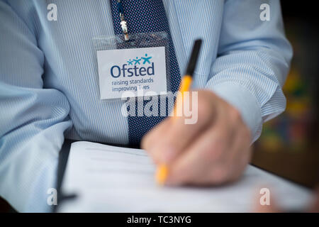 A man dressed in a shirt and tie with an Ofsted lanyard appears to be compiling a report using a pen and clipboard. (Editorial use only) Stock Photo