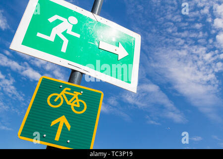 Emergency exit and bike route sign fixed on street lamp pole against blue sky Stock Photo