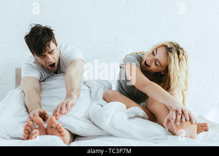 attractive blonde woman and handsome man yawning in bed Stock Photo