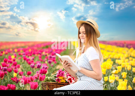 Beautiful young woman reading book in tulip field on spring day Stock Photo