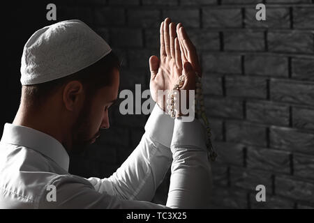 Young Muslim man praying against dark brick wall Stock Photo