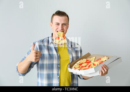 Handsome man eating tasty pizza on light background Stock Photo