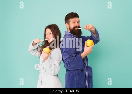 Oral hygiene. Couple bathrobes hold toothbrushes and apples. Personal hygiene. Couple in love cleaning teeth. Freshness and cleanliness. Keep teeth healthy. Healthy habits. Brush teeth every morning. Stock Photo