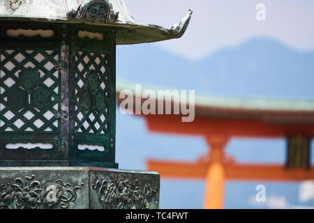 A traditional lantern stands in the foreground while the vermilion torii (shrine gate) at Itsukushima Jinja rises in the background. Stock Photo