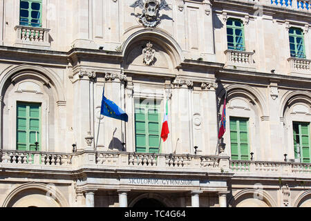 Close up picture capturing the front side facade of historical building of public Catania University in Sicily, Italy. On the balcony there are waving Italian flag and flag of European Union. Stock Photo