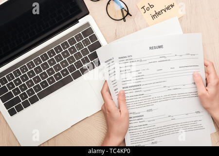 cropped view of recruiter holding resume templates near sticky note with job interview lettering and laptop Stock Photo