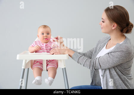 Mother feeding her little baby on grey background Stock Photo