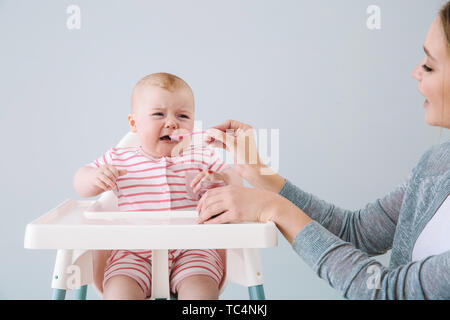 Mother feeding her little baby on grey background Stock Photo