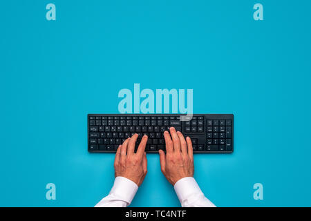 Top view of male hands using black compute keyboard. Over blue background. Stock Photo