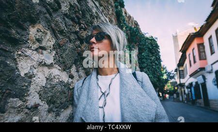 Fashionable young woman in the streets of Antalya. Beautiful blonde adult female standing against wall. Stock Photo