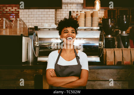 Woman barista inside her coffee shop. Woman bartender in cheerful mood standing in front on the counter. Stock Photo