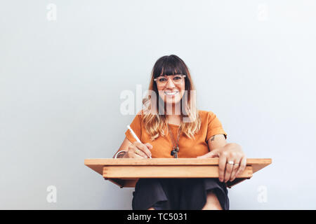 Close up of an illustrator sitting with a pad holding a drawing pen. Portrait of a woman sitting on floor with a drawing pad making a sketch. Stock Photo