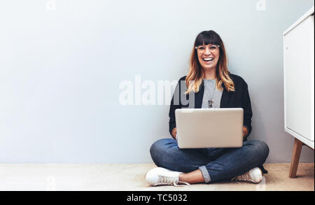 Woman entrepreneur working on laptop sitting at home. Smiling woman sitting on the floor at home using a laptop computer. Stock Photo