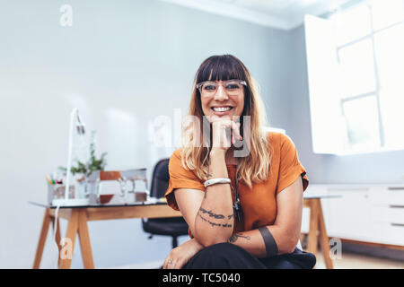 Portrait of a cheerful businesswoman sitting in office with her hand to her chin. Smiling woman entrepreneur taking a break enjoying her time in offic Stock Photo