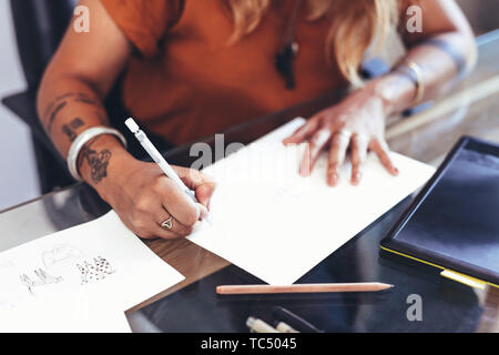 Close up of hands of an artist making a drawing on a paper. Cropped shot of a female artist making a design on a drawing paper. Stock Photo