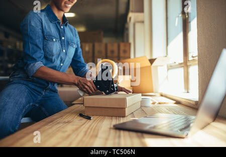 Woman packing cardboard box using tape dispenser. Female entrepreneur preparing the shipment for delivery. Stock Photo