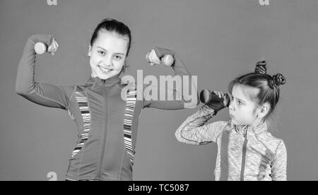 Girls cute kid exercising with dumbbells. Motivation and sport example concept. Toddler repeat exercise after sister. Sport exercises for kids. Healthy upbringing. Sporty babies. Following her sister. Stock Photo