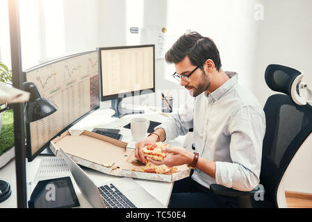 I love pizza Young bearded businessman or trader in eyewear and formal clothes is eating hot pizza while sitting in his modern office. Coffee break. Food concept. Business concept. Trade concept