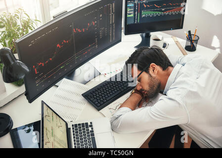 I need to relax. Tired young bearded trader in formal wear sleeping on the desk while working late in his modern office. Trade concept. Investment concept. Rest concept Stock Photo