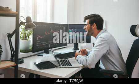 Great Happy young businessman or trader in formalwear looking at charts on computer screen in the office and smiling. Stock exchange. Financial trading concept. Investment concept Stock Photo