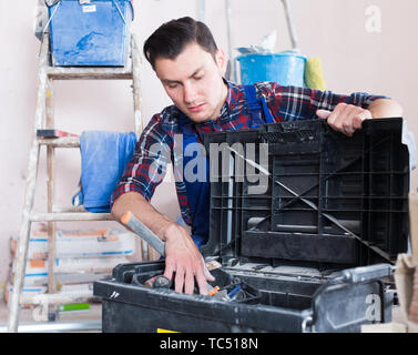Young builder handyman choosing necessary tool in toolbox Stock Photo