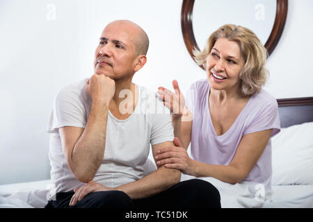 Positive mature  girlfriend consoling grieving man sitting apart Stock Photo