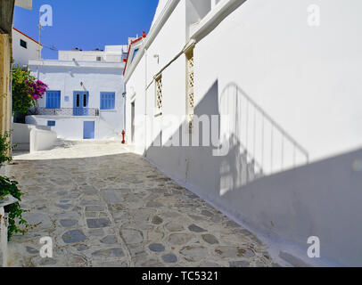 Beautiful peaceful stone paved empty alley, white houses with blue windows at noon time balcony shadow and fire hydrant Tinos island, Greece. Stock Photo