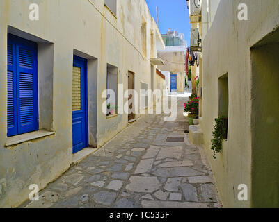 Beautiful peaceful stone paved empty alley with white houses with blue windows at noon time, Tinos island, Greece. Stock Photo