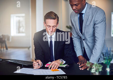 Two diverse businessmen going over notes and documents while working together at a desk in an office Stock Photo