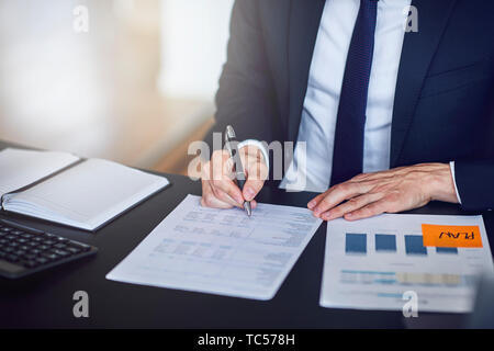 Closeup of a businessman going over paperwork while sitting at his desk in a bright modern office Stock Photo