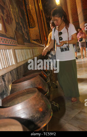 Thai woman deposits coins as offering in a bowl of a monk at Wat Pho, Temple of the Reclining Golden Buddha, Grand Palace, Bangkok, Thailand. Stock Photo