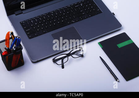 Close-up of comfortable working place in office with laptop, mouse, notebook, glasses, pen and other equipment laying on table with copy space. Top Stock Photo