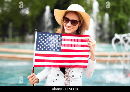 Young patriot woman in hat smilig and stretching USA flag in park and celebrating Indendence day, 4th of July Stock Photo