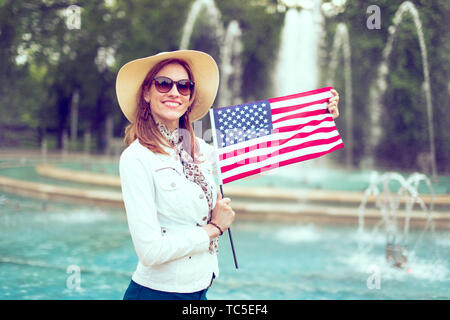 Happy young patriot woman in hat stretching USA flag in park, Independence Day, Fourth of July Stock Photo