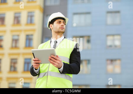 Portrait of Mixed Race engineer holding digital tablet standing at construction site outdoors, copy space Stock Photo