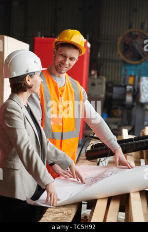 Waist up portrait of two smiling workers discussing plans standing in indusrial workshop Stock Photo