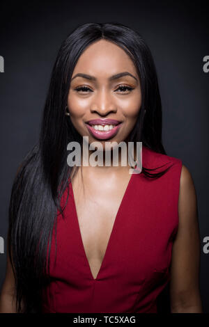 Portrait of a Black African American female wearing a red outfit on a dark background.  She is happy and smiling. Stock Photo