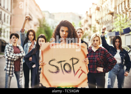 Stop War Make Peace. Young woman is holding a banner with word stop it while standing on the road during a women's march in front of female activists. Women rights. Women's march. Human rights Stock Photo
