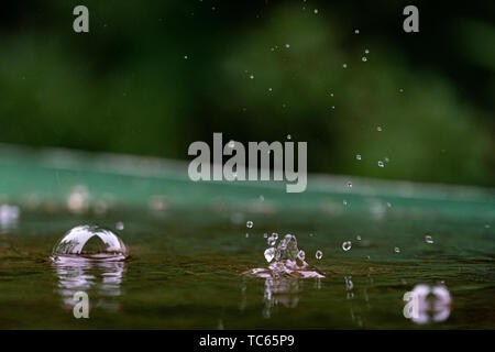 raindrops and water bubbles in a puddle on a green table with bokeh background Stock Photo