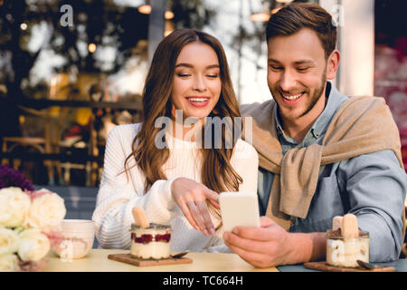 cheerful man sitting with happy girl pointing with finger at smartphone Stock Photo