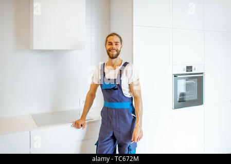 Portrait of a handyman in uniform standing in the renovated kitchen at home Stock Photo