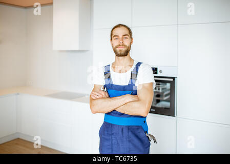 Portrait of a handyman in uniform standing in the renovated kitchen at home Stock Photo
