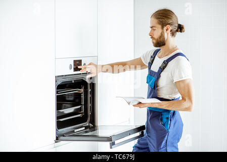 Handsome workman in overalls setting up electric oven on the kitchen at home Stock Photo