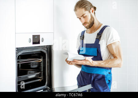 Handsome workman in overalls setting up electric oven on the kitchen at home Stock Photo