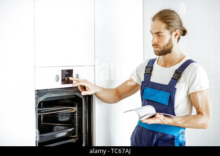 Handsome workman in overalls setting up electric oven on the kitchen at home Stock Photo
